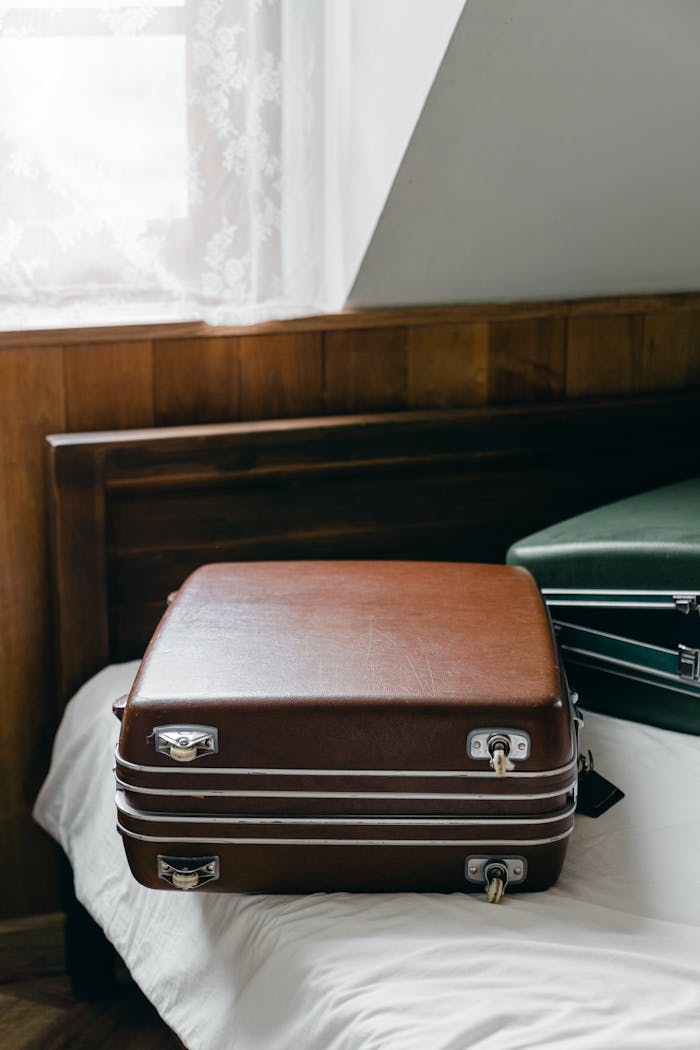 Home From above of elegant leather brown and green suitcases placed on edge of bed in light room under sloping roof