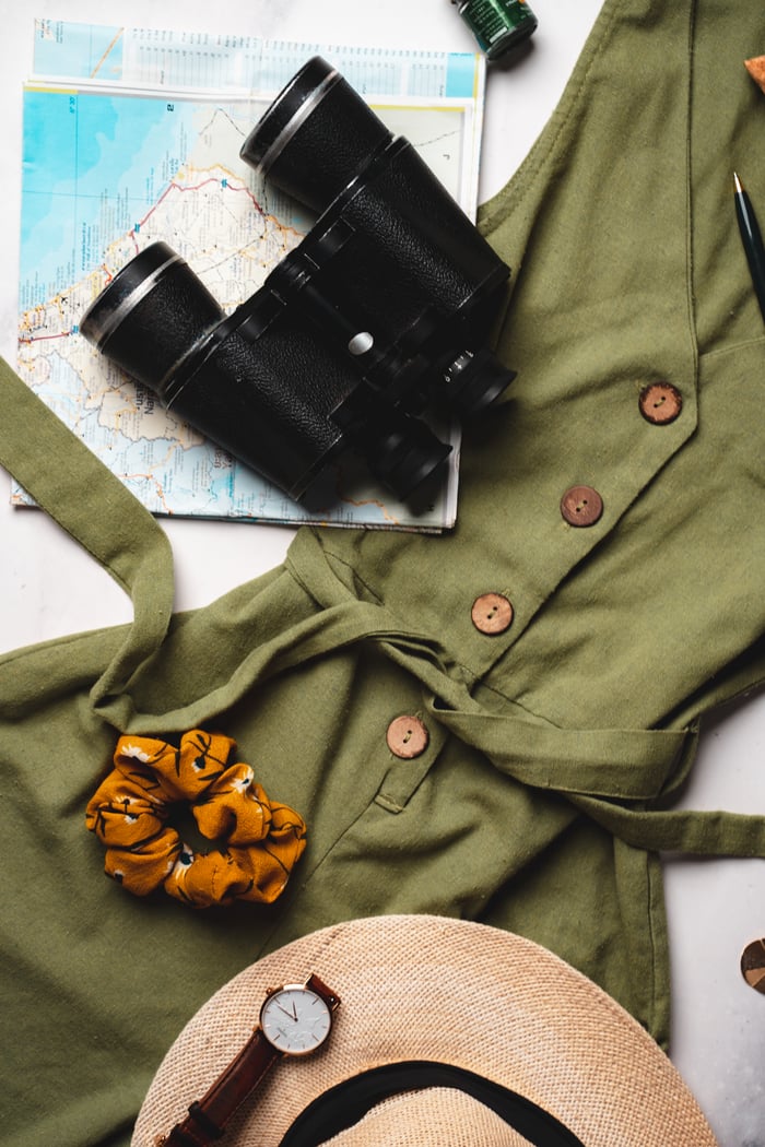 Home Flat lay of army green dress, binoculars, map, and travel items for adventure planning.