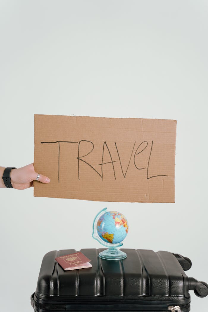 Home Creative travel concept featuring a cardboard sign, globe, passport, and suitcase against a white background.